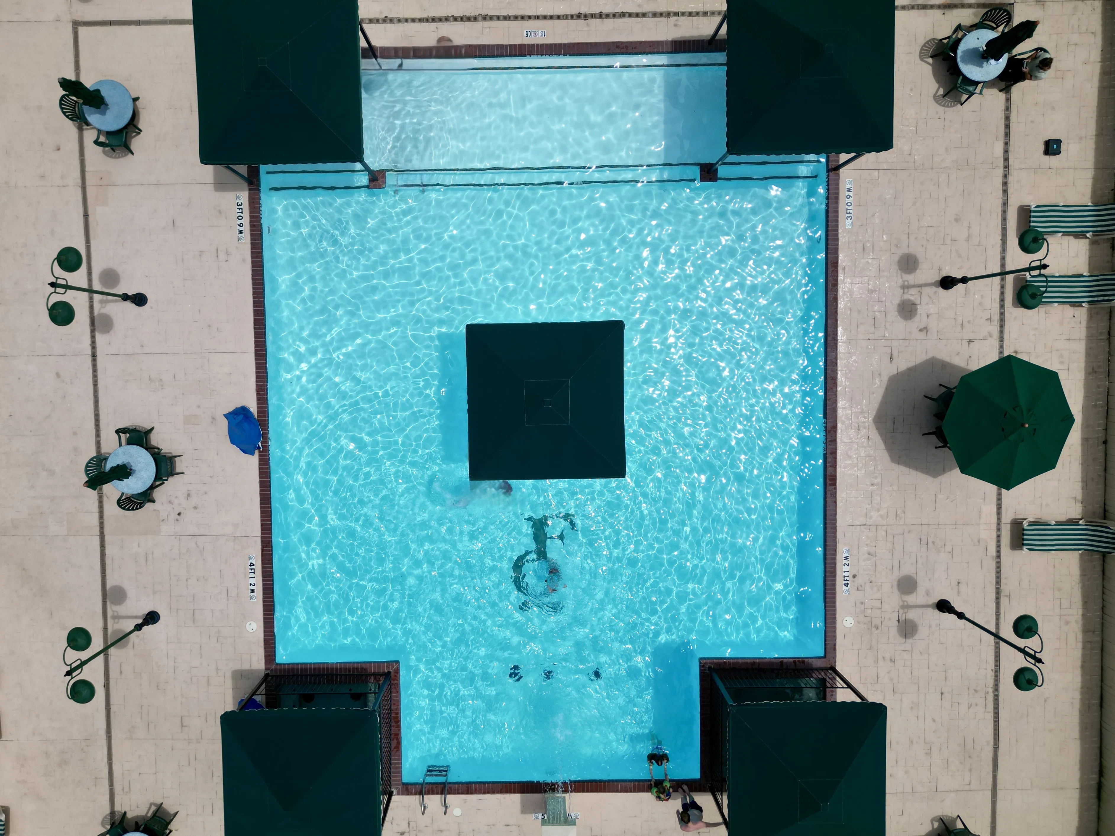 Aerial view of a clear blue swimming pool with surrounding lounge chairs and green umbrellas.